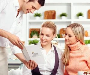 Ein sthender Mann ziegt zwei sitzenden Frauen eine Liste