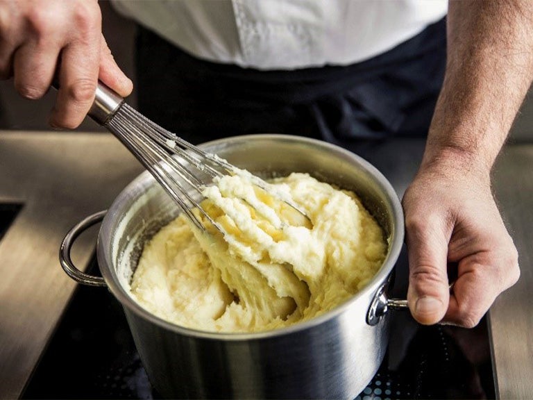 Topf mit Kartoffel Pürree wird mit Schneebesen gerührt