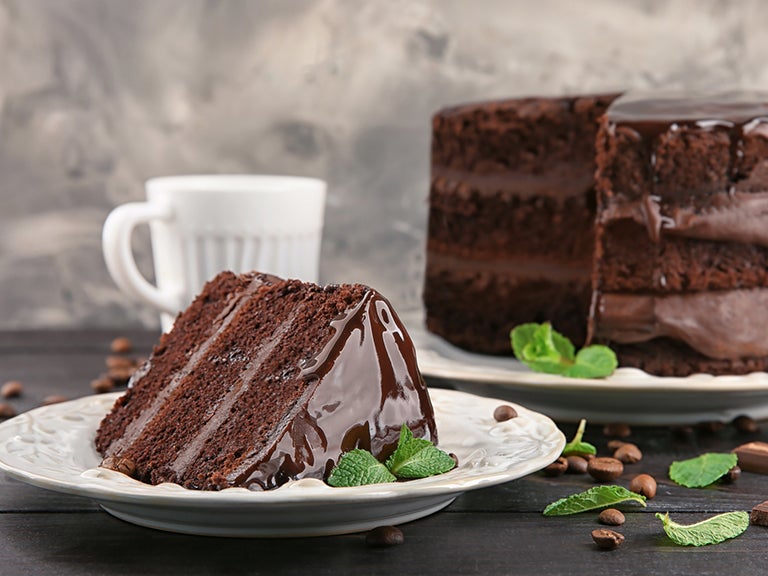 Kuchenstück mit Schokoladenkuchen und Tasse im Hintergrund