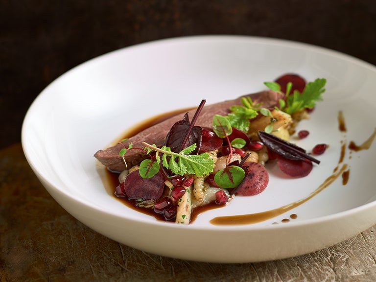 Fleischgericht mit Beilage, präzise angerichtet und dekoriert.