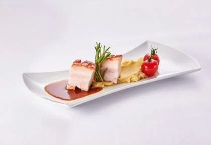 Lackierter Spanferkelbauch auf Garam-Perlzwiebelpüree auf einem weißen Teller