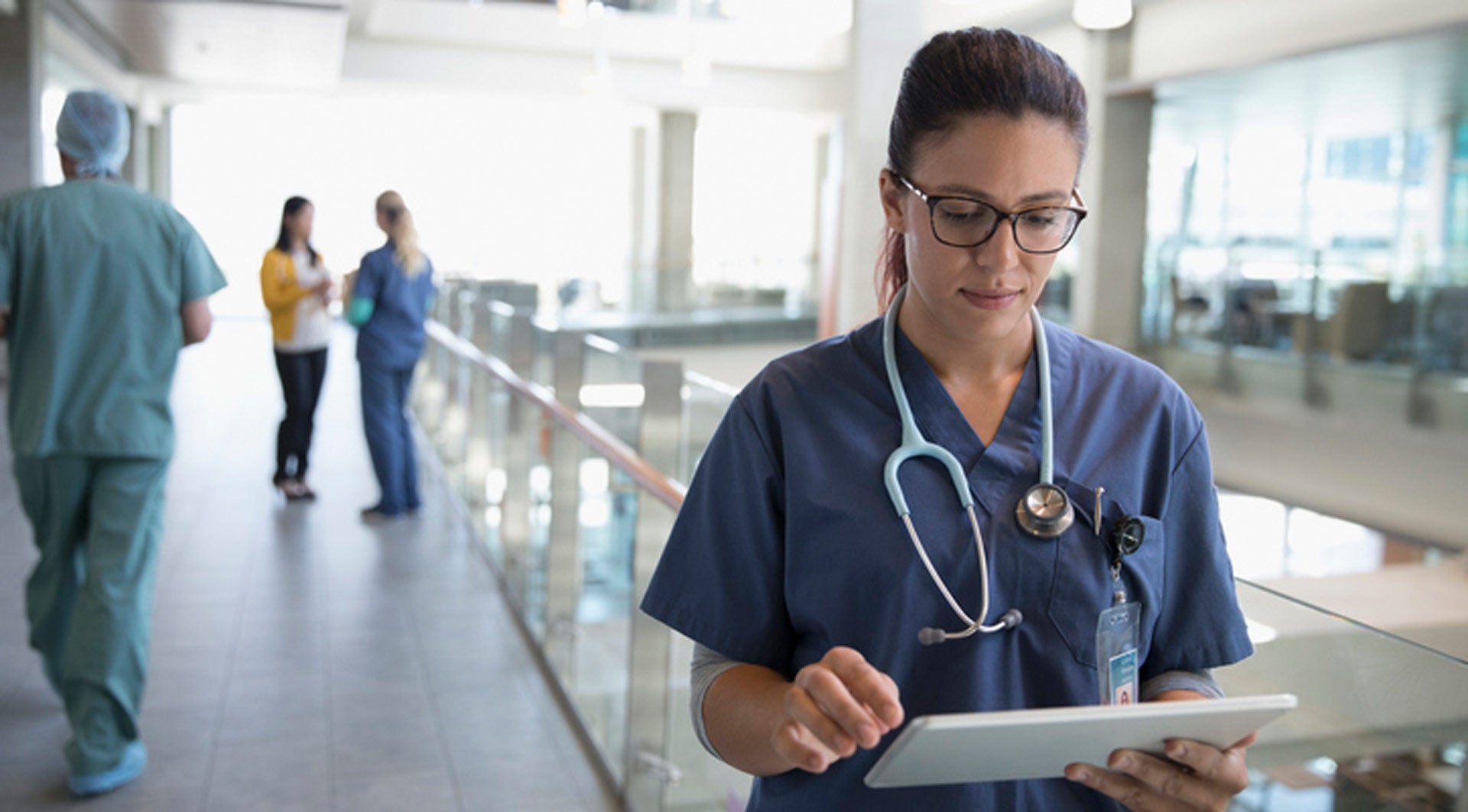 Ärztin mit Brille und Stetoskop schuat runter auf notebook in Krankenhaus