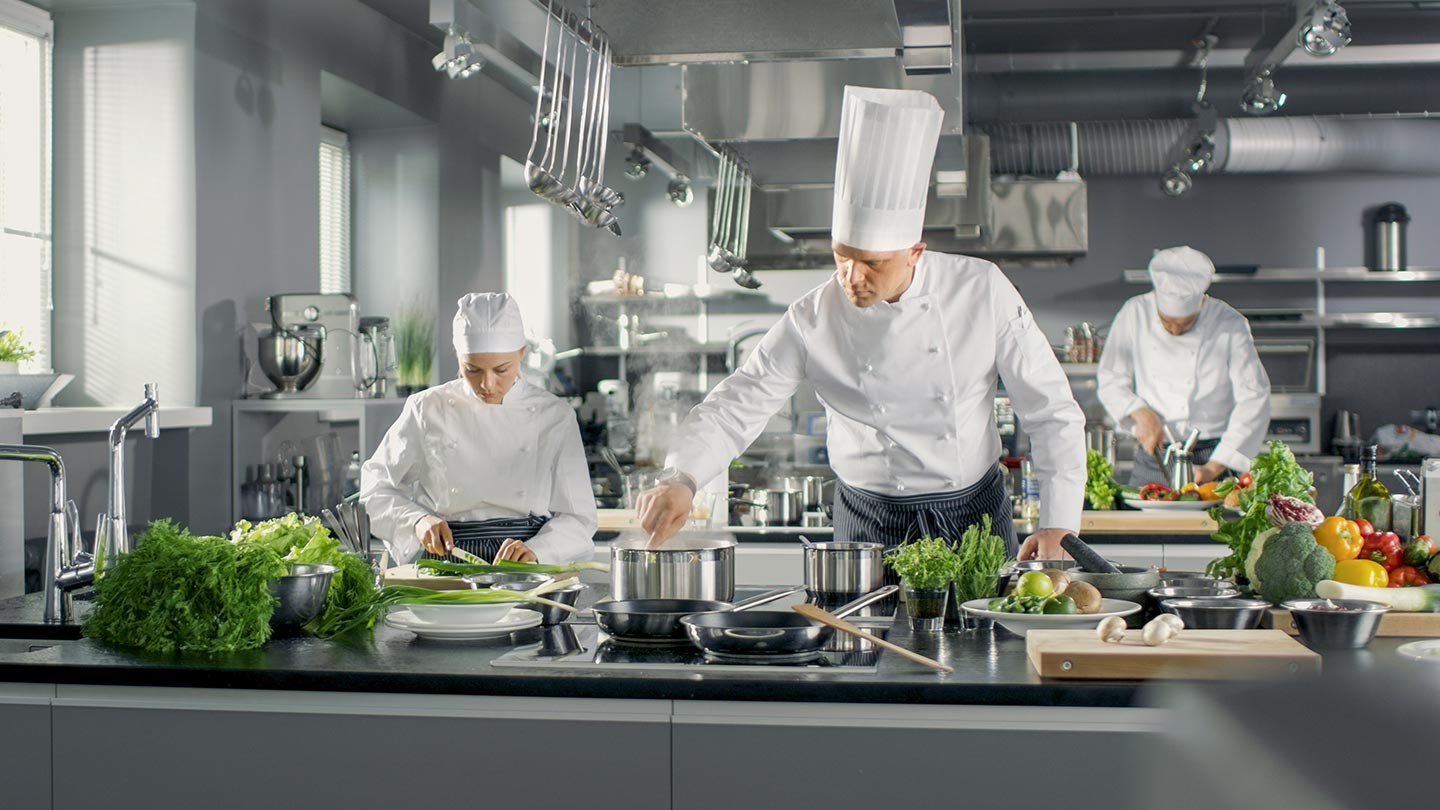 Berühmter Koch arbeitet in einer großen Restaurantküche. Die Küche ist voll von Essen und Gemüse