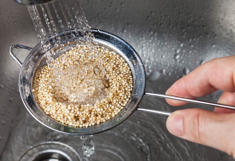 Mann hält kleine Siebrippen mit rohen Quinoa-Samen