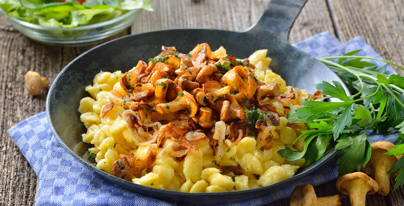 Schwäbische Spätzle mit frischen, gebratenen Pfifferlingen und Zwiebeln in der Pfanne rustikal serviert