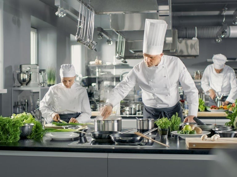 Berühmter Koch arbeitet in einer großen Restaurantküche. Die Küche ist voll von Essen und Gemüse